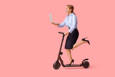 Diz üstü bilgisayarı olan, pembe arka planda elektrikli scooter süren olgun bir iş kadını.