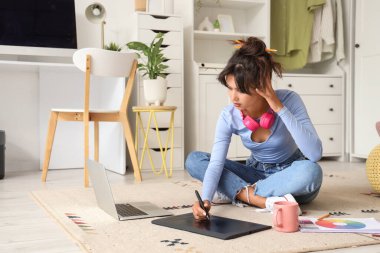 Düşünceli kadın grafik tasarımcısı evde halıda tabletle çalışıyor.