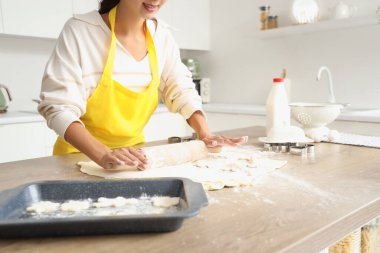 Genç bir kadın mutfaktaki masaya hamur döküyor.