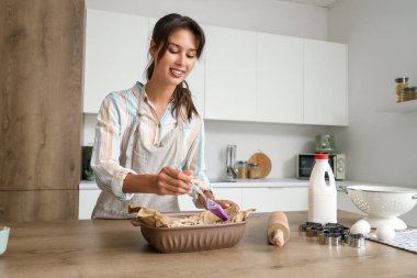 Genç bir kadın mutfakta haşhaşlı çörekleri yağlıyor.