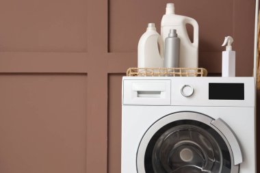 Çamaşır deterjanları kahverengi duvarın yanındaki çamaşır makinesinde.