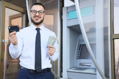Bankamatik yakınlarında kredi kartı ve dolar banknotları olan bir iş adamı.