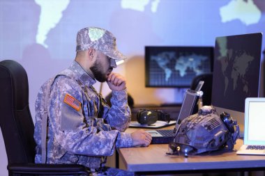 Askerî laptopla çalışan düşünceli asker geceleri masada oturuyor.