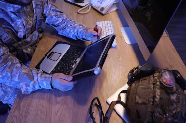 Askeri laptopla çalışan bir asker geceleri masa başında çalışıyor.