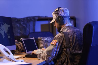 Asker, askeri laptopla çalışıyor. Geceleri ofiste, arka planda.