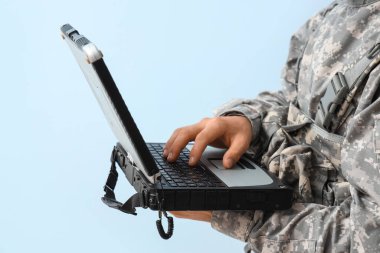 Genç asker hafif arka planda askeri dizüstü bilgisayarla çalışıyor, yakın plan.