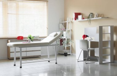 Kanepesi, masası ve raf ünitesi olan jinekoloğun ofisi.