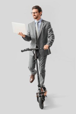 Diz üstü bilgisayarı olan yakışıklı bir iş adamı, arka planda elektrikli scooter kullanıyor.