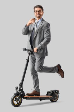 Açık arkaplanda elektrikli scooter kullanan yakışıklı bir iş adamı.