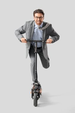 Hafif arka planda elektrikli scooter kullanan yakışıklı bir iş adamı.