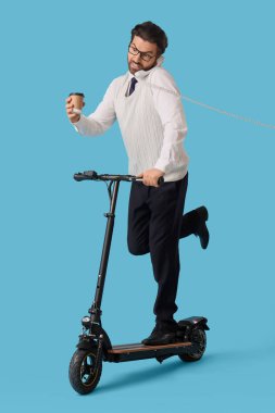 Kahveli ve elektrikli scooterlı yakışıklı iş adamı mavi arka planda telefonla konuşuyor.