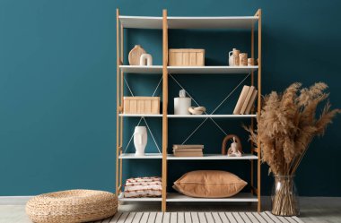 Süslü dekorlu kitaplık ve mavi duvarın yanında otlar.