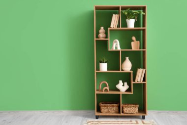 Odada yeşil duvarın yanında bitki ve dekor olan bir kitaplık.