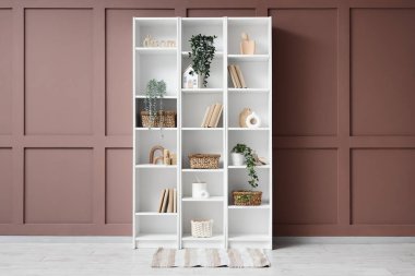 Hasır sepetli kitaplık ve odada kahverengi duvarın yanındaki bitkiler.