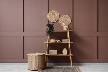 Odadaki kahverengi duvarın yanında bitki ve hasır sepetli kitaplık.
