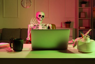 İnsan iskeleti modeli karanlık ofiste masa başında sohbet ediyor.