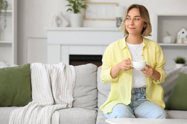 Evdeki kanepede bir fincan kahveyle oturan güzel kadın.