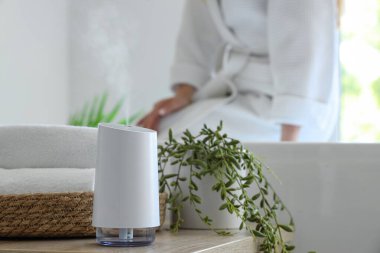 Havluları ve bitkileri olan hava nemlendirici banyoda oturan kadına karşı, yakın plan.