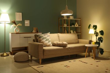 Geceleri karanlık oturma odasının içinde kanepe, raf ünitesi ve parlayan lambalar.