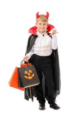 Cadılar Bayramı için giyinmiş, beyaz arka planda hediye çantaları olan küçük bir çocuk.