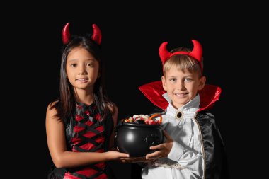 Cadılar Bayramı için giyinmiş küçük çocuklar ve siyah arka planda şekerler.