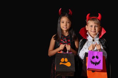 Cadılar Bayramı için giyinmiş küçük çocuklar ve siyah arka planda hediye çantaları.