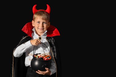 Cadılar Bayramı için giyinmiş, siyah arka planda şekerleri olan küçük bir çocuk.
