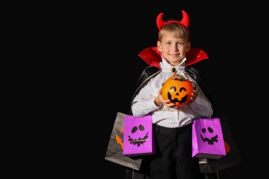 Cadılar Bayramı için giyinmiş küçük bir çocuk ve siyah arka planda hediye çantaları.