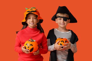 Cadılar Bayramı için giyinmiş küçük çocuklar ve turuncu arka planda şekerler.