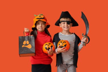 Cadılar Bayramı için giyinmiş çocuklar ve turuncu arka planda hediye paketleri.