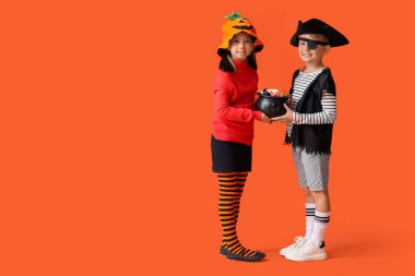 Cadılar Bayramı için giyinmiş küçük çocuklar ve turuncu arka planda şekerler.