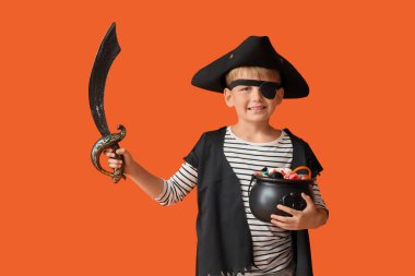 Cadılar Bayramı 'nda korsan gibi giyinmiş, turuncu arka planda şekerler olan küçük çocuk.