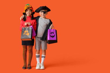 Cadılar Bayramı için giyinmiş küçük çocuklar ve turuncu arka planda hediye çantaları.