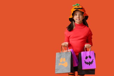 Cadılar Bayramı için giyinmiş şirin Asyalı kız. Turuncu arka planda hediye çantaları var.