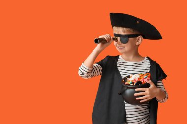 Cadılar Bayramı 'nda korsan gibi giyinen küçük çocuk, turuncu arka planda şeker ve dürbün taşıyor.