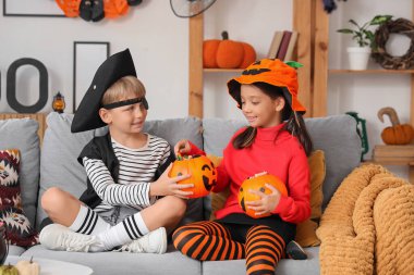 Cadılar Bayramı için giydirilmiş küçük çocuklar ve evdeki kanepede oturan şekerler.