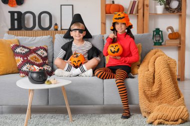 Cadılar Bayramı için giydirilmiş küçük çocuklar ve evdeki kanepede oturan şekerler.