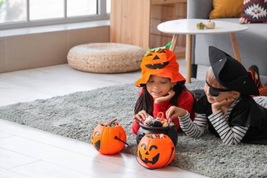 Cadılar Bayramı için giyinmiş küçük çocuklar ve evde halı üzerinde uzanan şekerler.