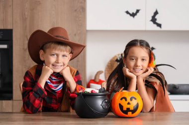 Cadılar Bayramı için giyinmiş küçük çocuklar ve mutfak masasında şekerler.
