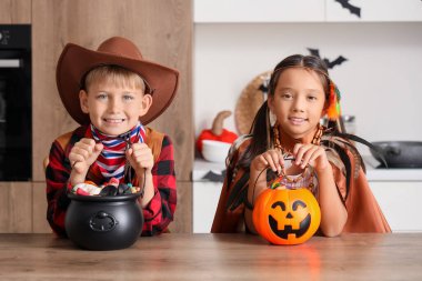 Cadılar Bayramı için giyinmiş küçük çocuklar ve mutfak masasında şekerler.