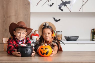 Cadılar Bayramı için giyinmiş küçük çocuklar ve mutfak masasında şekerler.