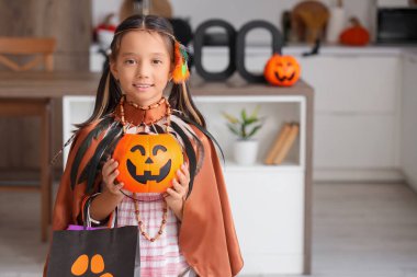 Cadılar Bayramı için giyinmiş tatlı Asyalı kız. Mutfakta şeker ve hediye çantaları var.