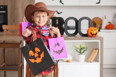 Cadılar Bayramı 'nda kovboy gibi giyinmiş küçük çocuk. Mutfakta hediye çantaları var.