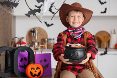 Cadılar Bayramı 'nda kovboy gibi giyinmiş küçük çocuk. Mutfaktaki masada şekerlerle.