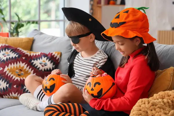 Cadılar Bayramı için giydirilmiş küçük çocuklar ve evdeki kanepede oturan şekerler.