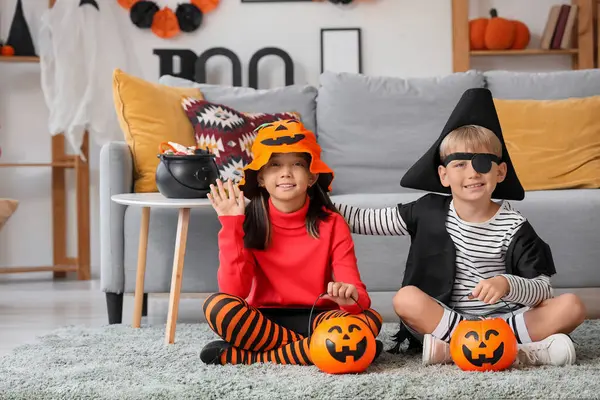 Cadılar Bayramı için giyinmiş küçük çocuklar ve evde halı üzerinde oturan şekerler.
