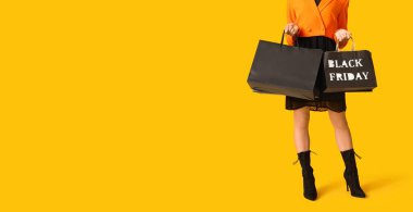 Sarı arka planda alışveriş torbaları olan genç bir kadın ve mesaj için yeri var. Kara Cuma indirimi