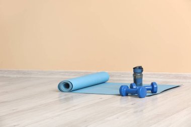 Spor salonundaki bej duvarın yanında halterli ve şişeli yoga minderi.
