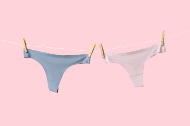 Pembe arka planda ipte sallanan kadın külotu.