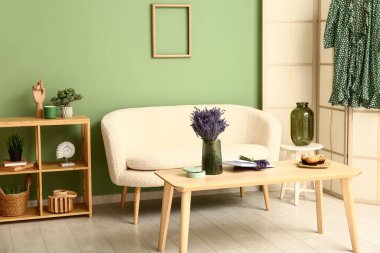 Katlanır ekran, raf ünitesi, kanepe, masa ve güzel lavanta çiçekleri olan şık bir oturma odası.